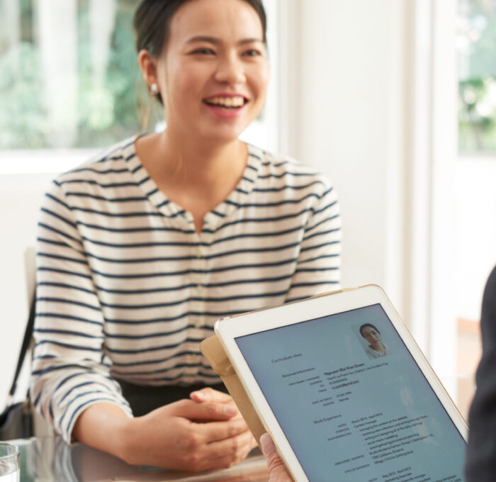 Female employee smiling during job interview, manager examining her resume on touchpad